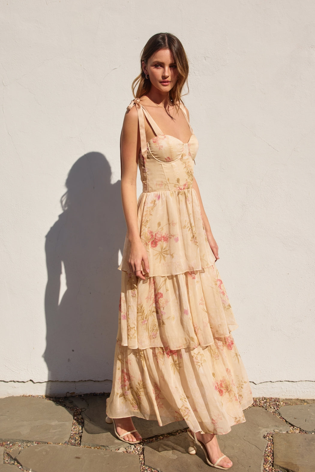 Woman wearing a floral dress standing against a white wall.