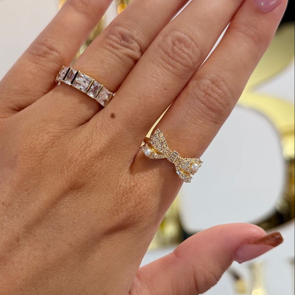 Hand wearing two rings with a blurred decorative background