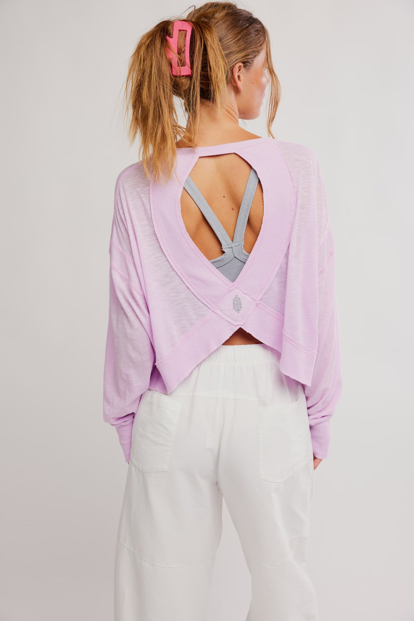 Woman wearing a light purple open-back top and white pants on a plain background
