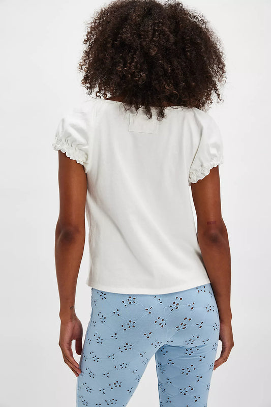 Person wearing a white top with ruffled sleeves and light blue pants with a subtle pattern on a plain background