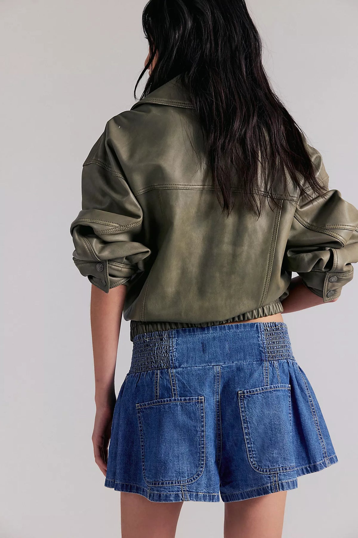 Person wearing a green jacket and blue denim skirt on a plain background