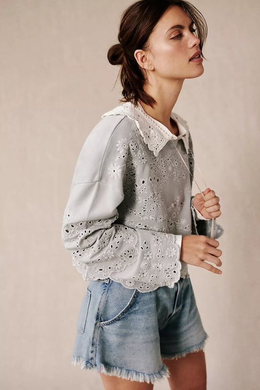 Woman wearing a light gray blouse with lace details and denim shorts against a beige background
