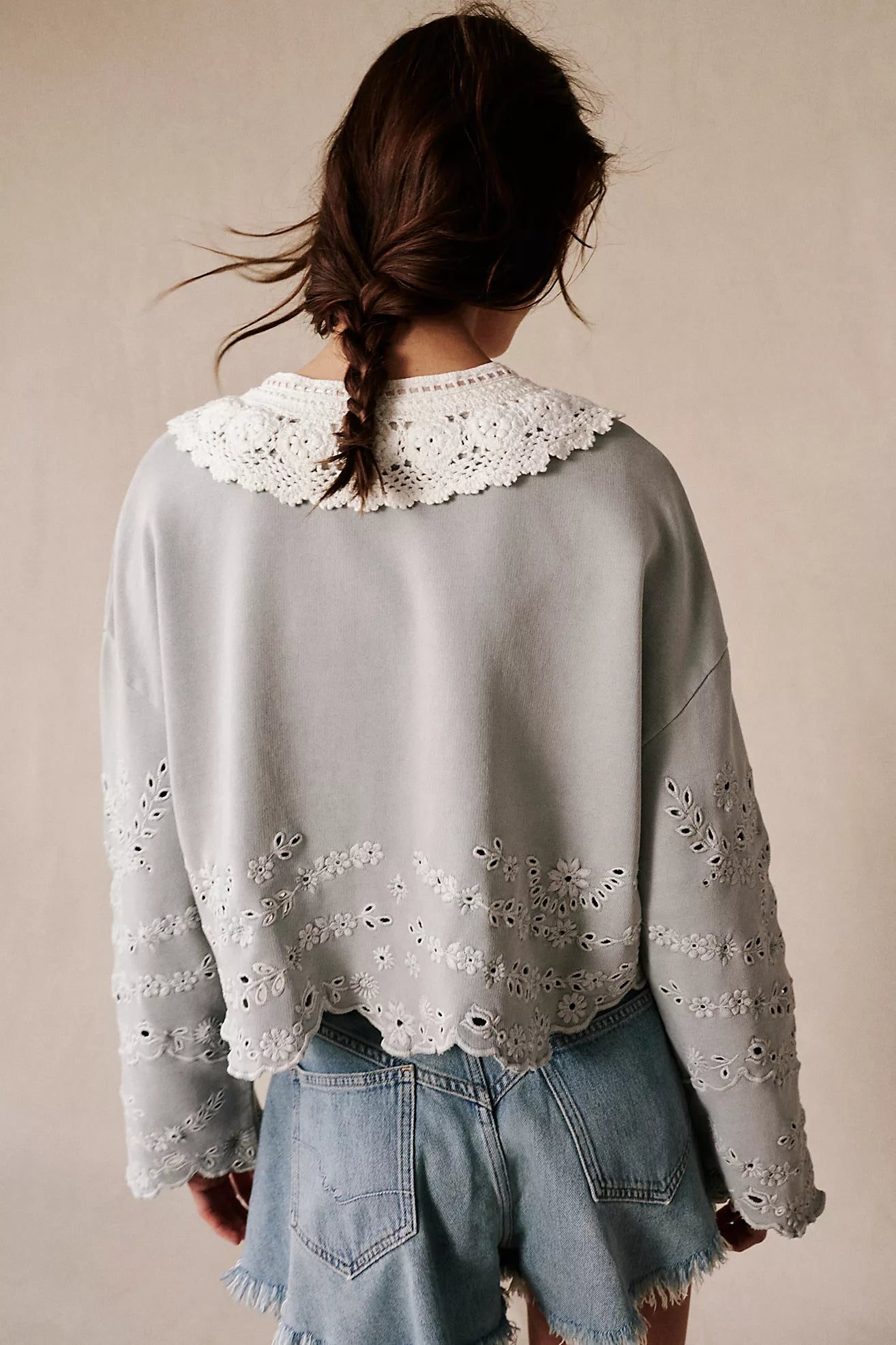 Person wearing a light gray sweater with lace details and denim shorts on a beige background