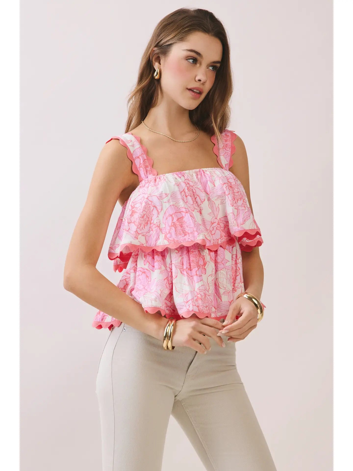 Woman wearing a pink floral top and beige pants against a light background