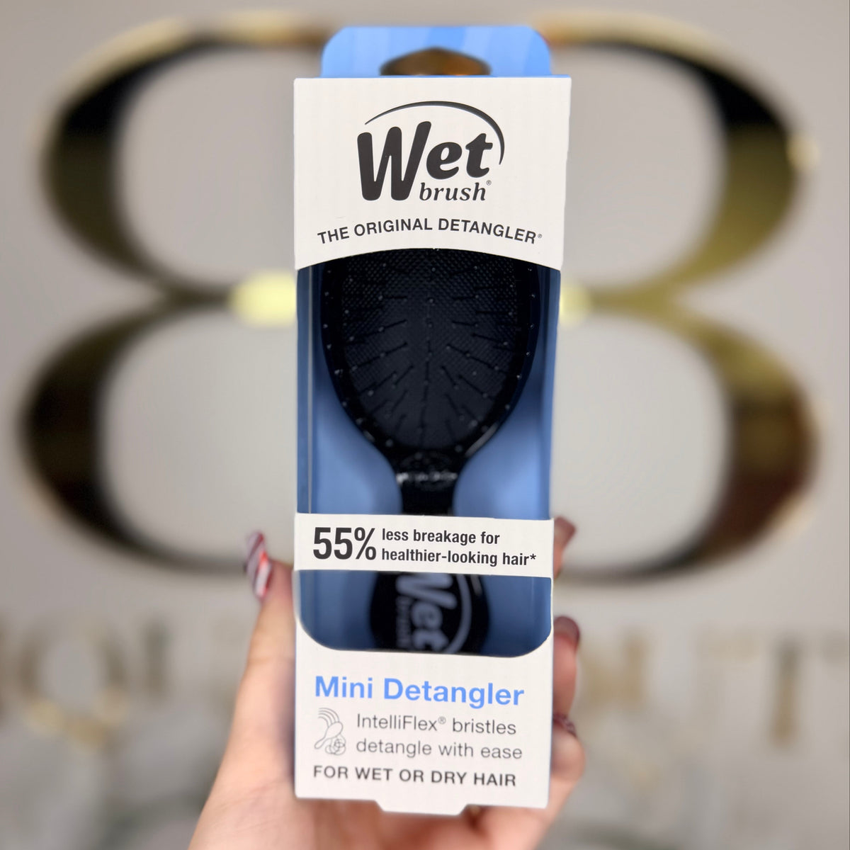 Hand holding a Wet Brush mini detangler packaging in front of a blurred background