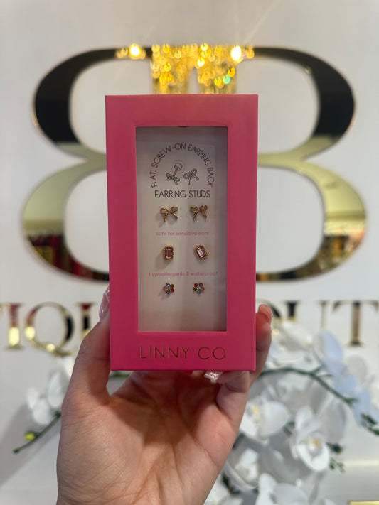 Hand holding a pink box with earrings inside, branded 'LINNY CO', against a decorative background.