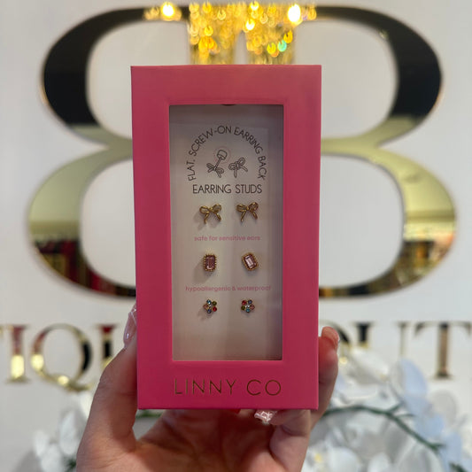 Hand holding a pink box with earrings inside, branded 'LINNY CO', against a decorative background.