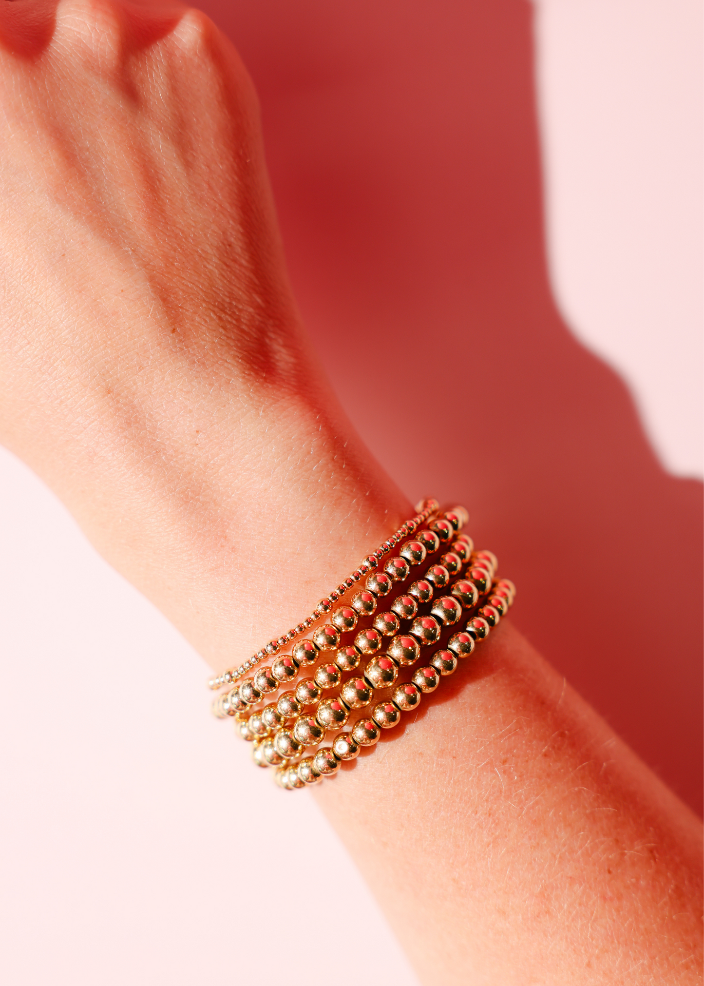 Gold beaded bracelets on a wrist with a soft pink background