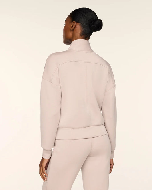 A model shown from the back wearing a matching light beige knit tracksuit, featuring a mock neck sweatshirt and coordinating pants, against a solid cream studio background.