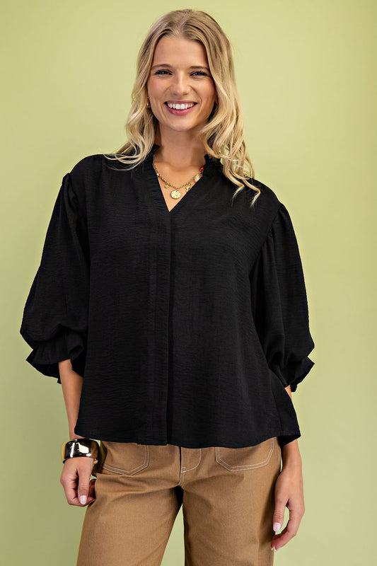 Woman wearing a black blouse and beige pants against a green background