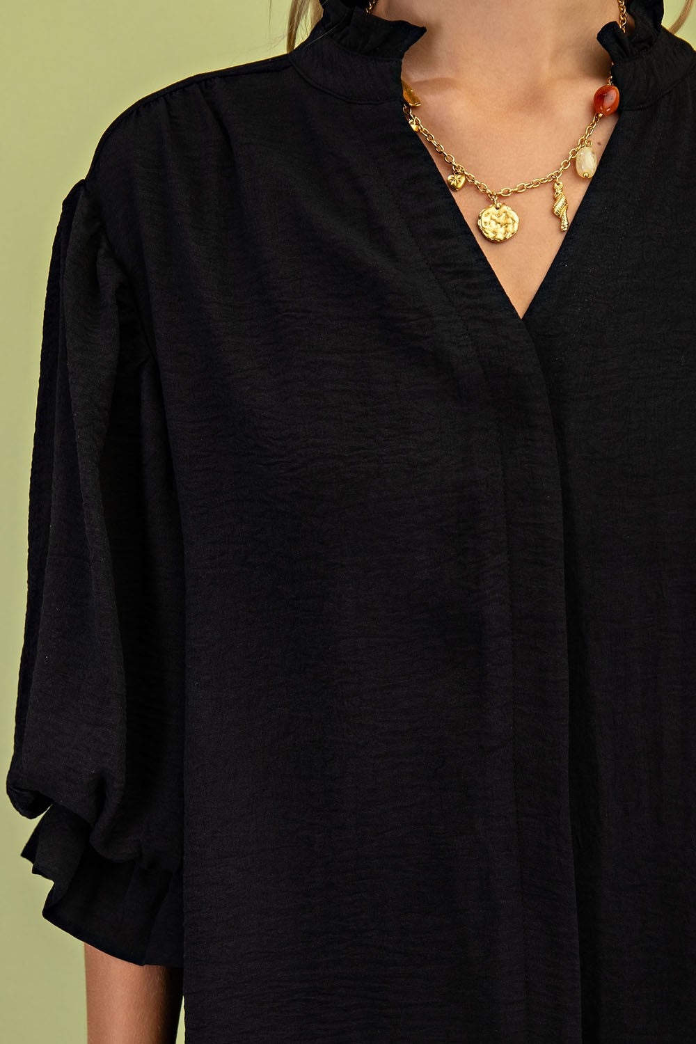 Person wearing a black outfit with gold jewelry on a green background