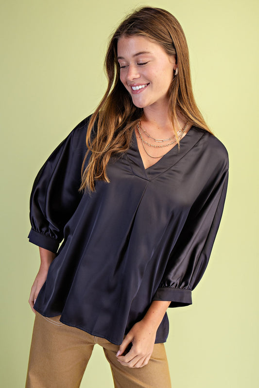 Woman wearing a black blouse with balloon sleeves against a light green background