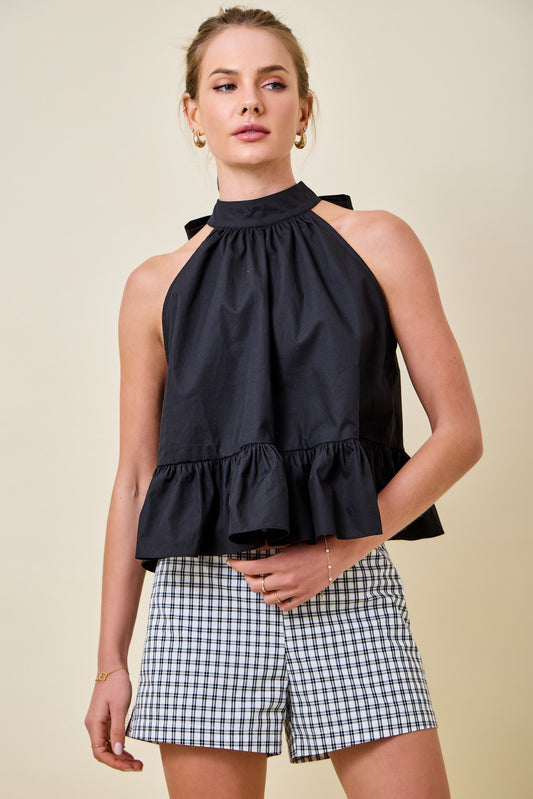 Woman wearing a black halter top and checkered shorts on a beige background