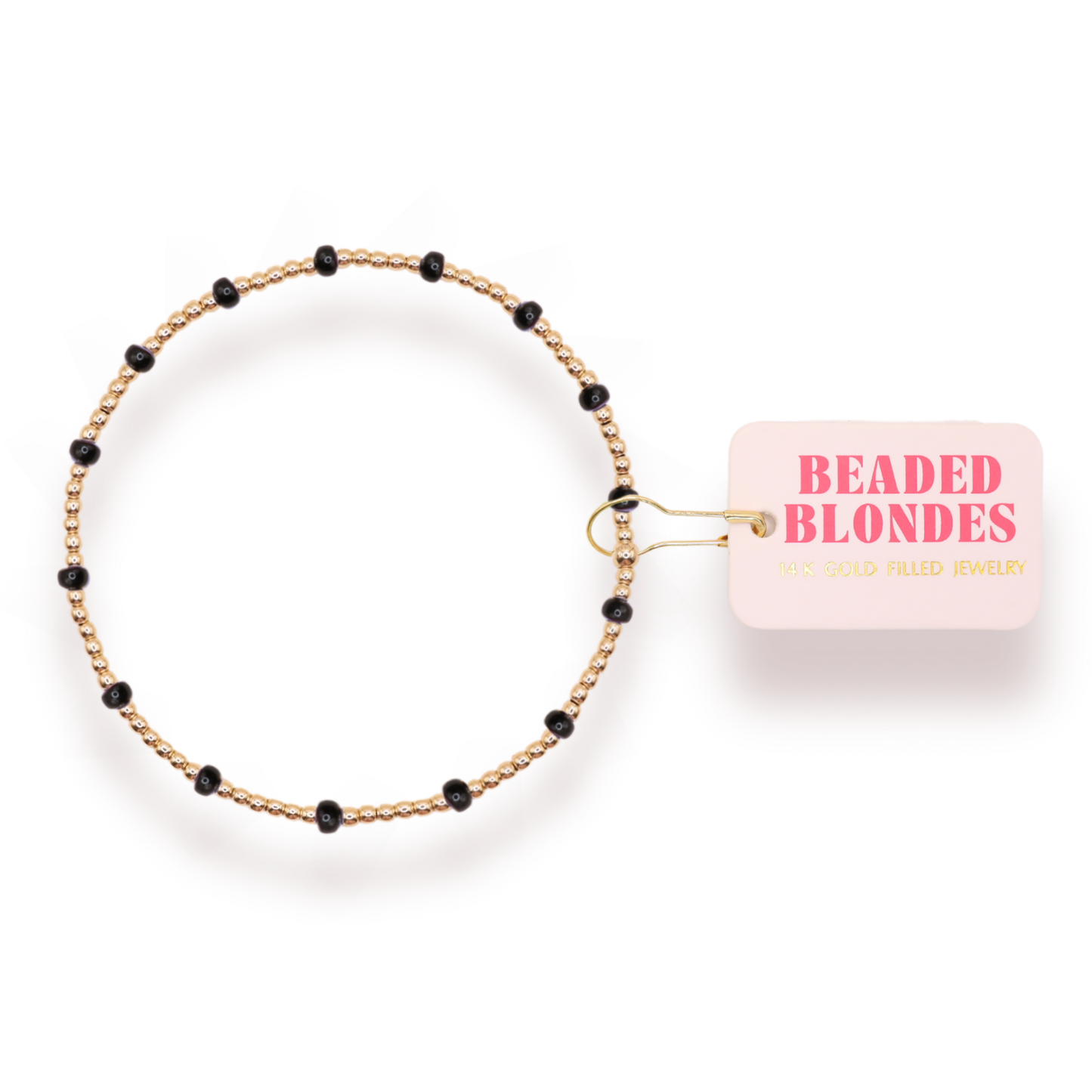 A delicate beaded bracelet with a gold-toned twisted wire base and small black beads spaced along the band, shown next to a light pink paper tag that reads 'BEADED BLONDES'.