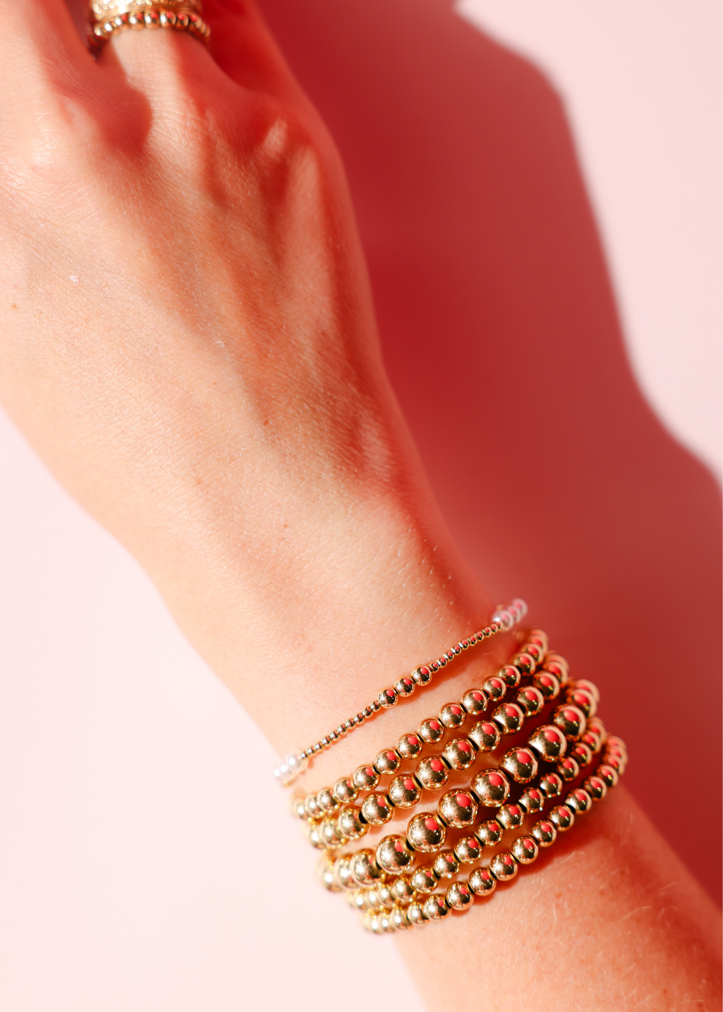 Gold beaded bracelet on a wrist with a soft pink background