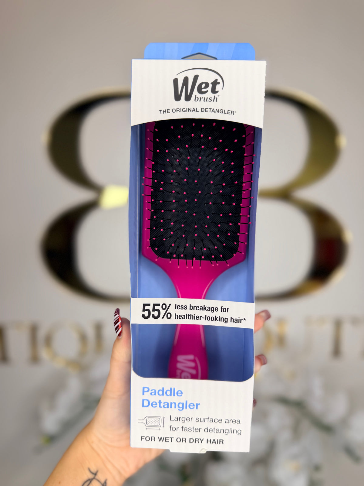 Wet brush paddle detangler packaging held by a hand with a blurred background