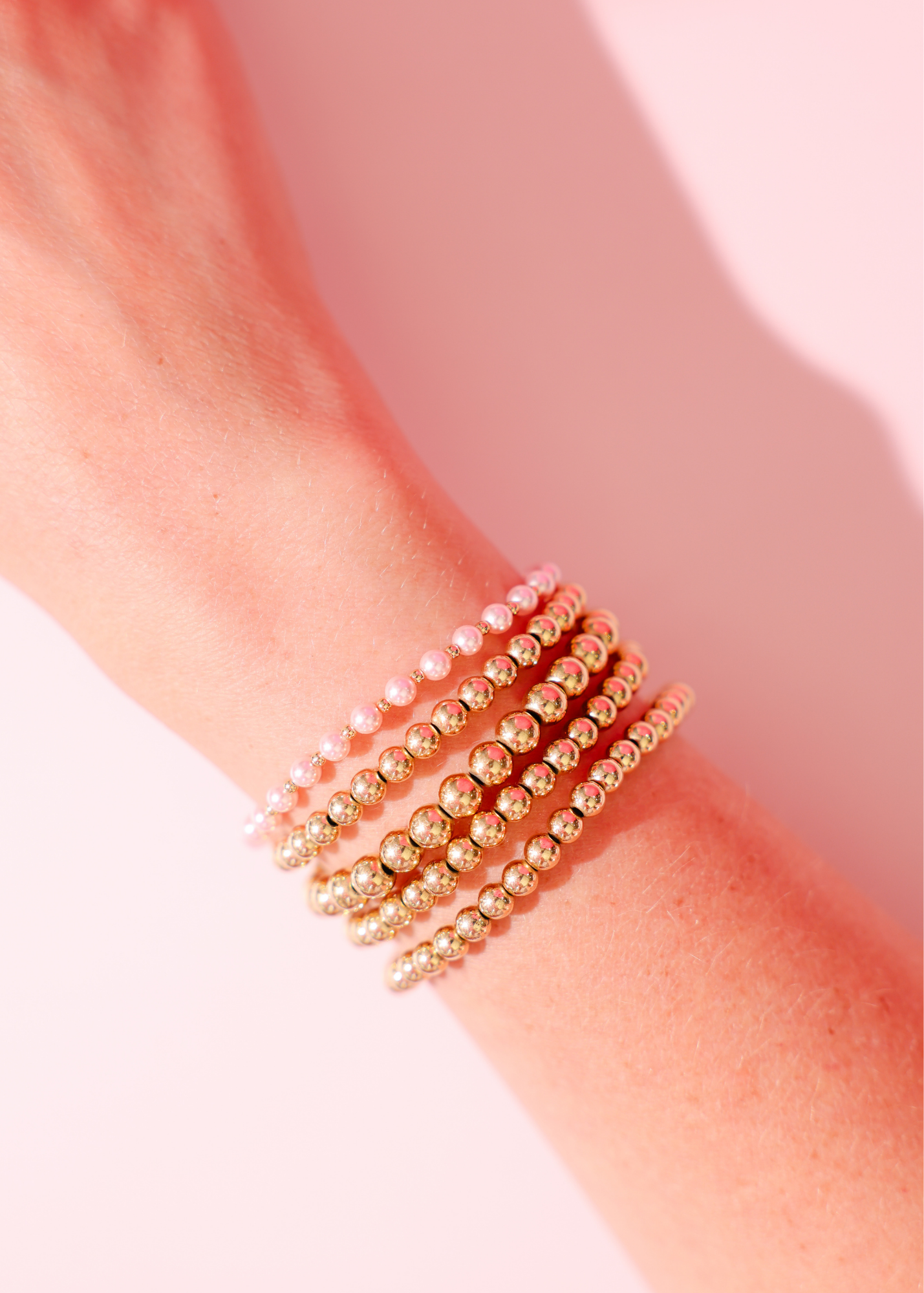 Gold beaded bracelet on a wrist with a soft pink background