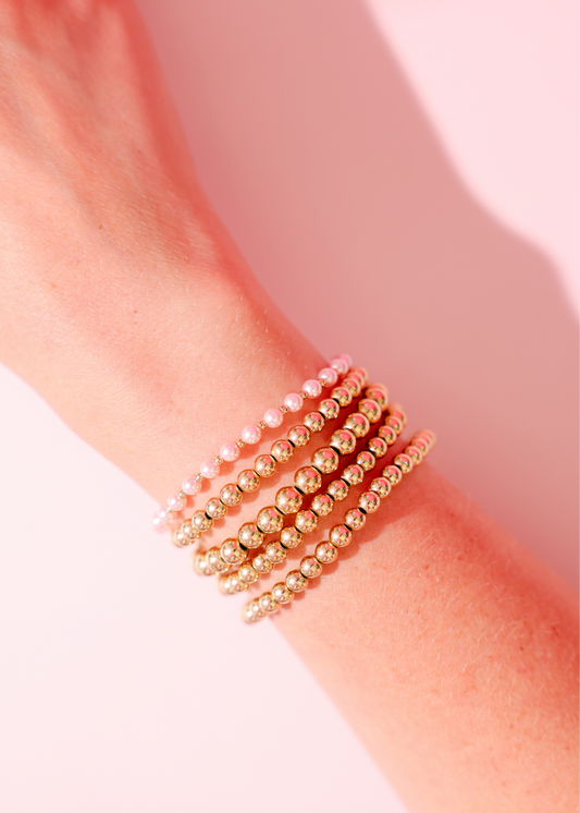 Gold beaded bracelet on a wrist with a soft pink background