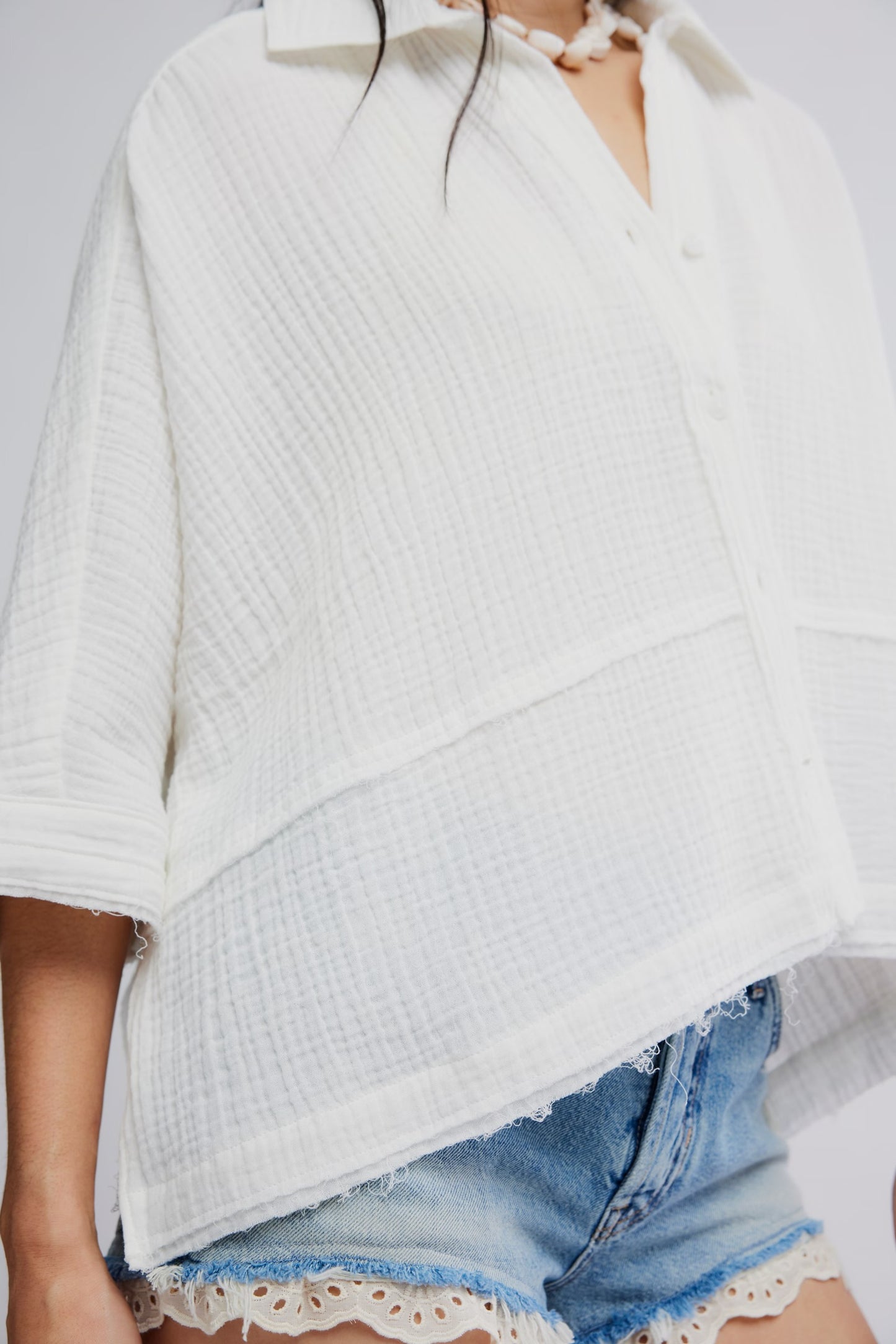 Person wearing a white textured sweater over a light blue dress with lace details.