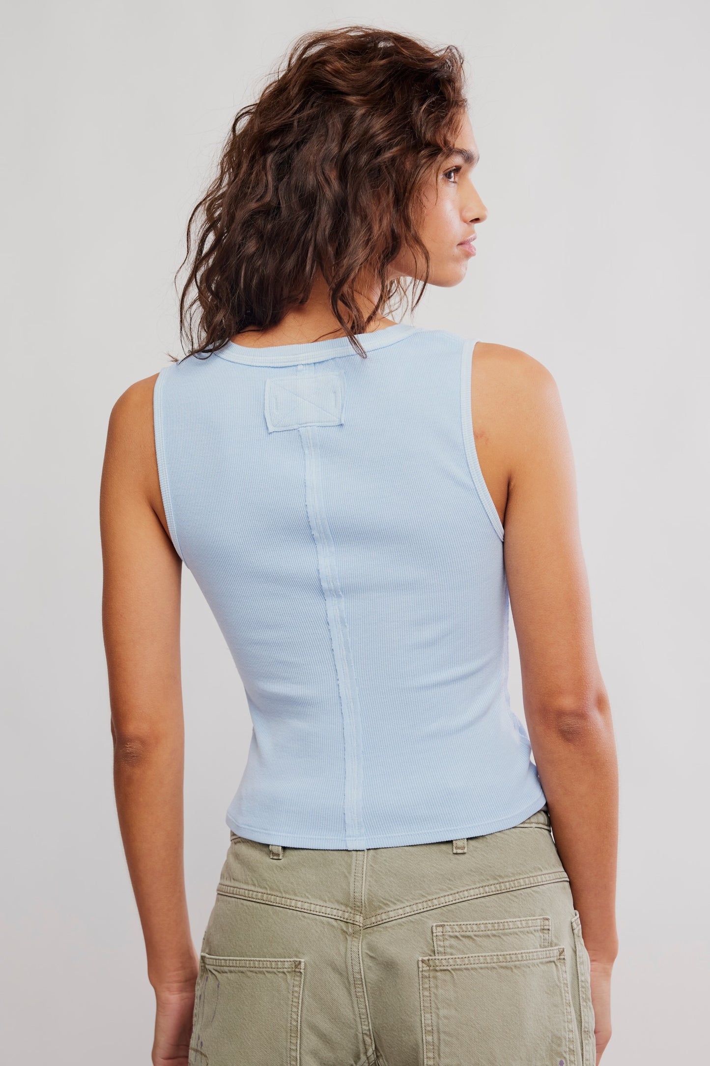 Woman wearing a light blue sleeveless top and green pants against a plain background