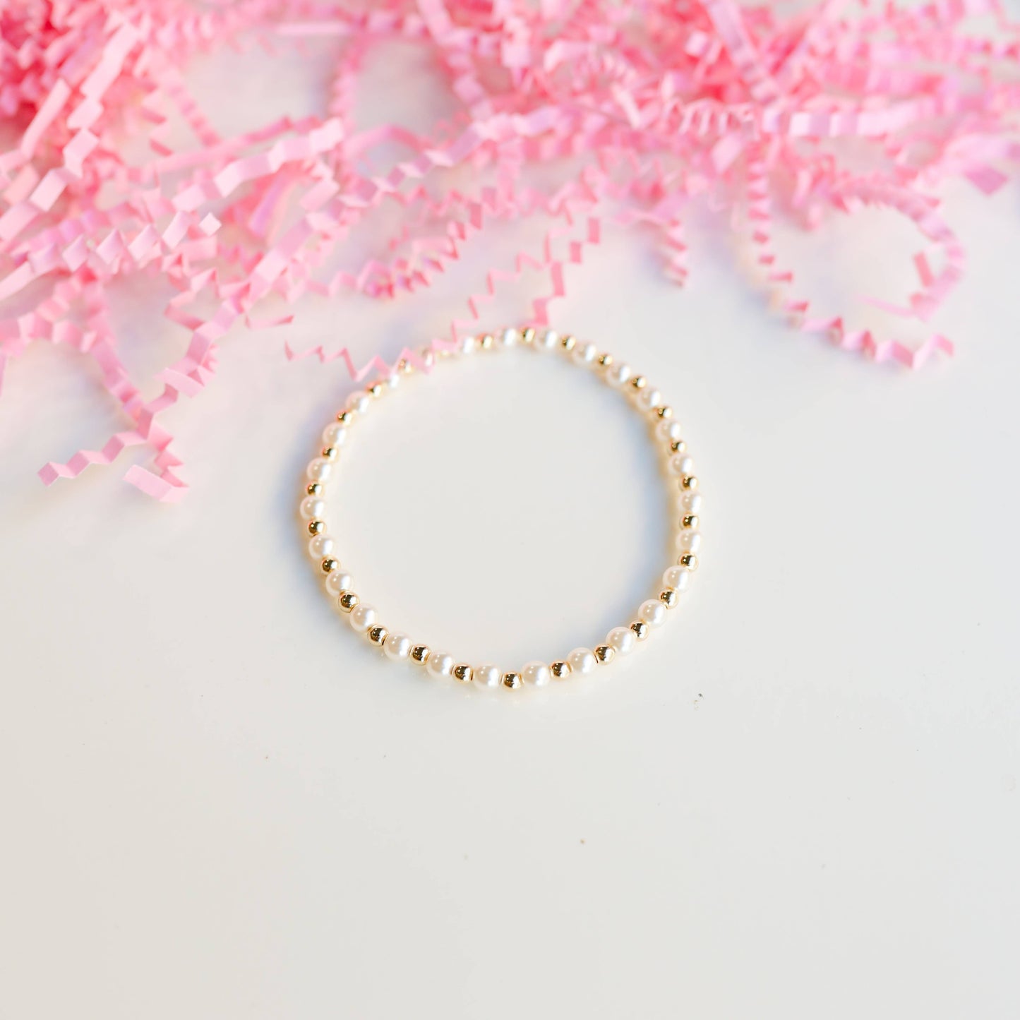 Gold bracelet on a white surface with pink decorative elements