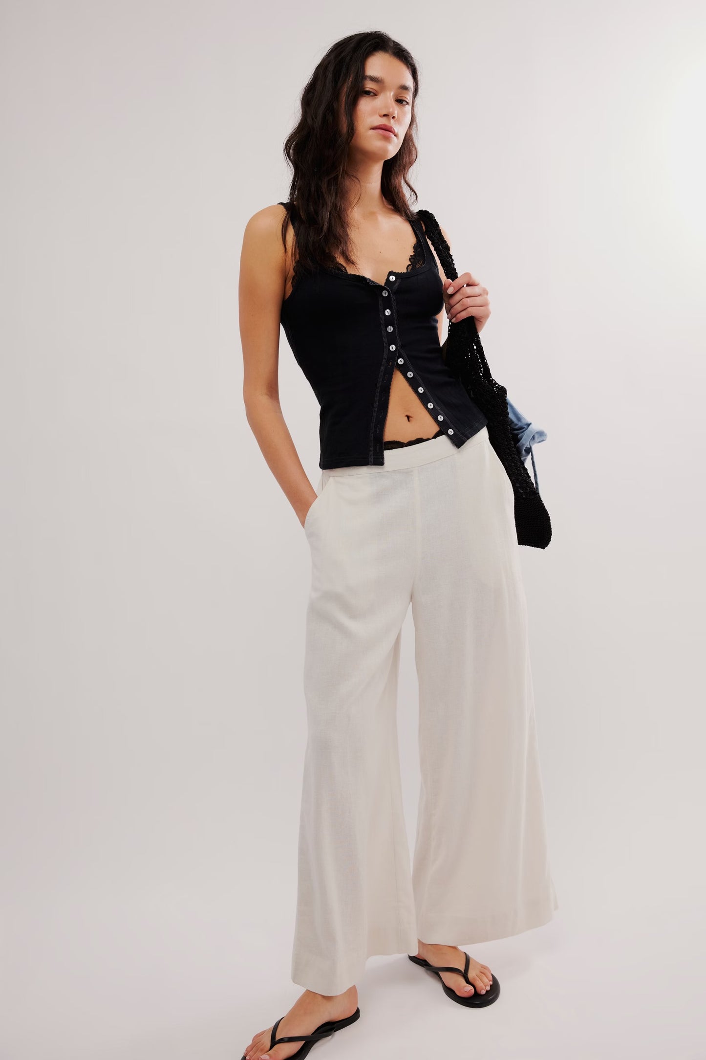 Woman wearing a black top with pearl details and white pants on a white background