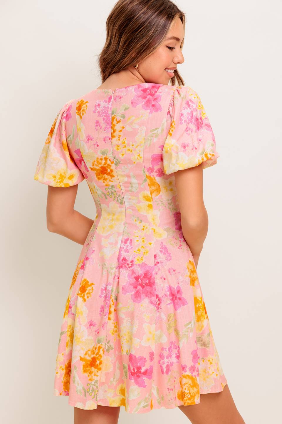 Woman wearing a floral dress with pink, yellow, and orange flowers on a plain background
