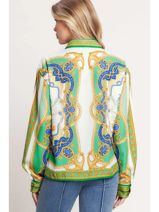 Woman wearing a patterned blouse with green, blue, and gold design on a plain background