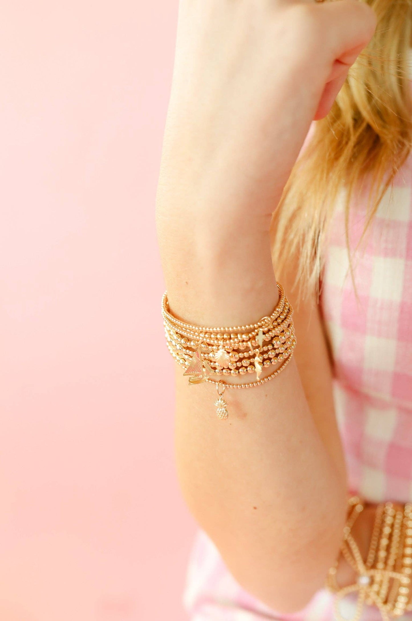 Close-up of a person's arm wearing multiple gold bracelets on a pink background