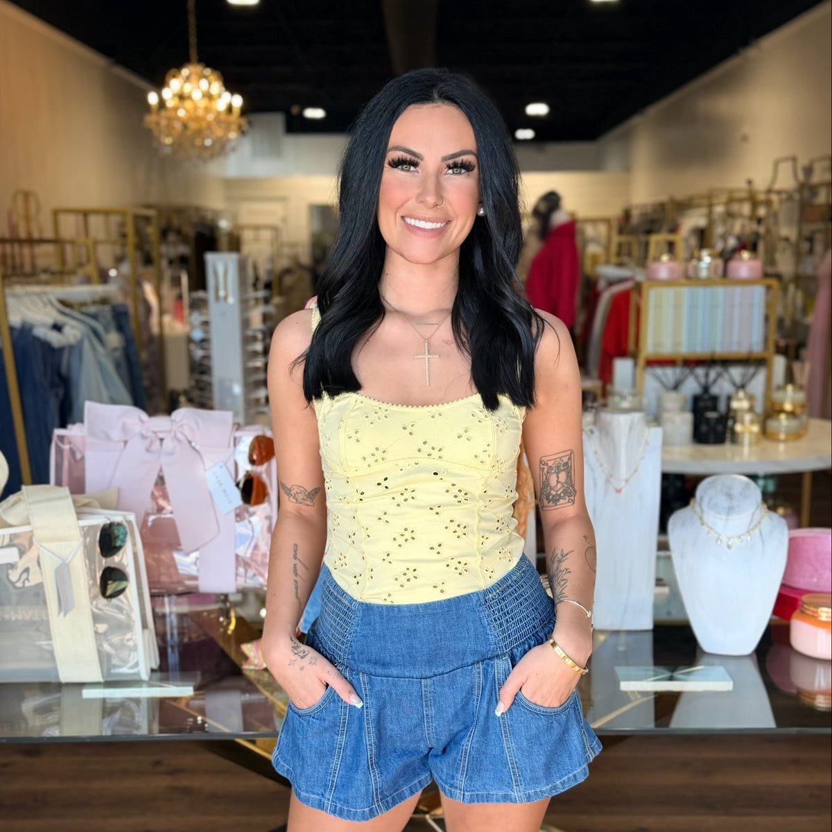 Model infront of store with yellow tank top and blue jean shorts