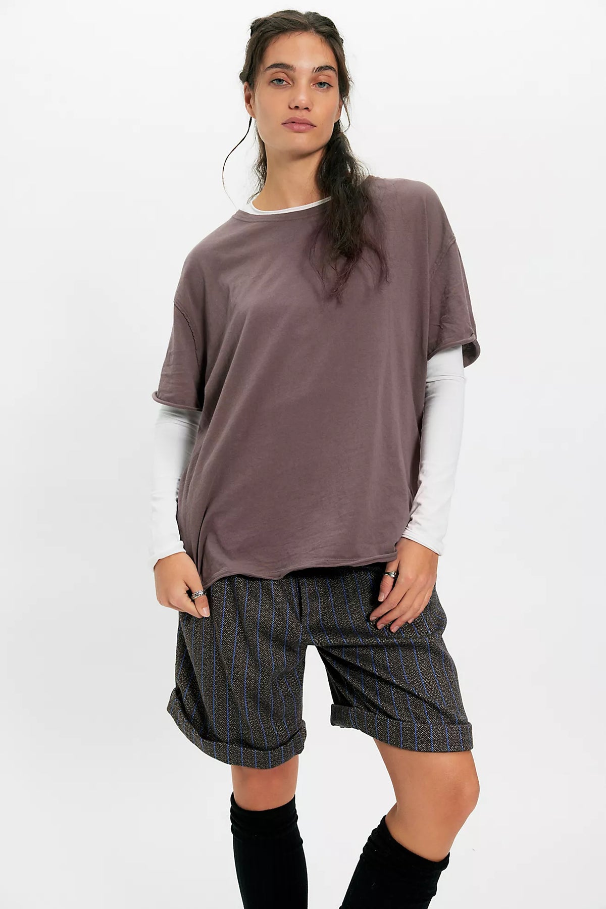 Woman wearing a loose-fitting brown top and plaid shorts on a white background