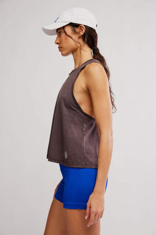 Woman wearing a brown tank top and blue shorts with a white cap on a light gray background