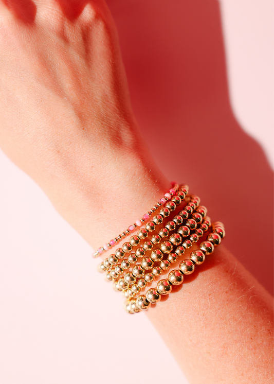 Gold beaded bracelets on a wrist with a blurred background