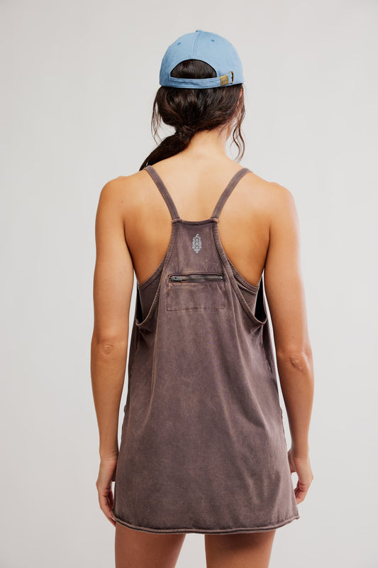 Person wearing a brown tank dress with a blue cap on a plain background