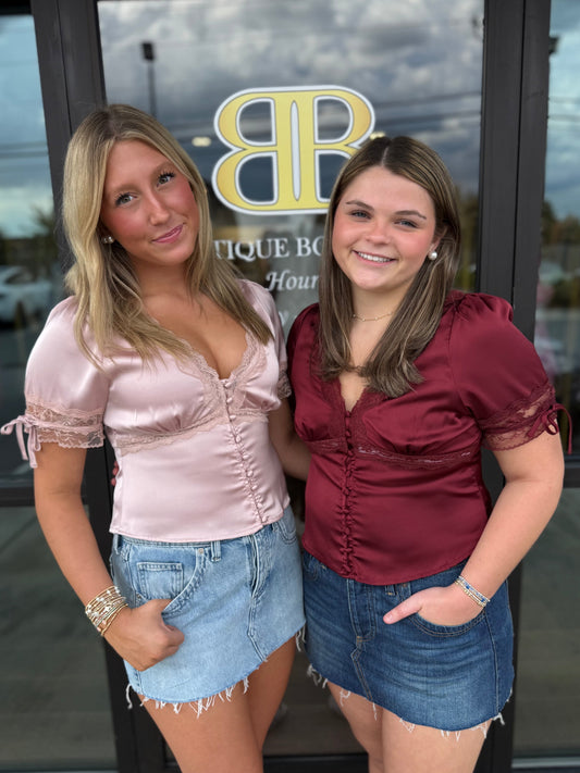 2 britique models wearing pink and maroon silk matching tops in front of store