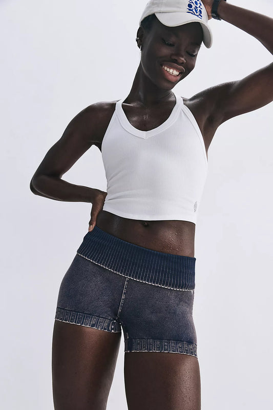 Person wearing a white tank top and blue denim shorts on a light gray background