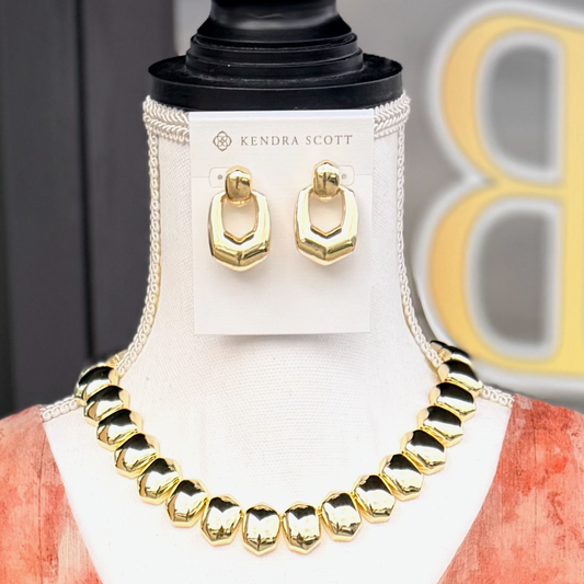 Gold necklace and earrings on a mannequin with Kendra Scott branding.