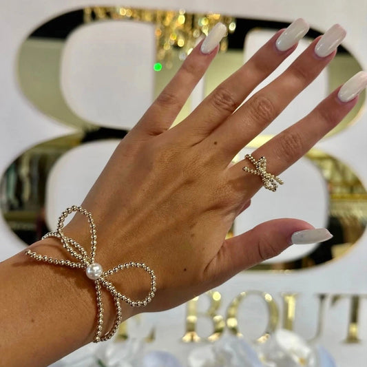 Gold and white beaded bow bracelet and bow ring shown on a hand.