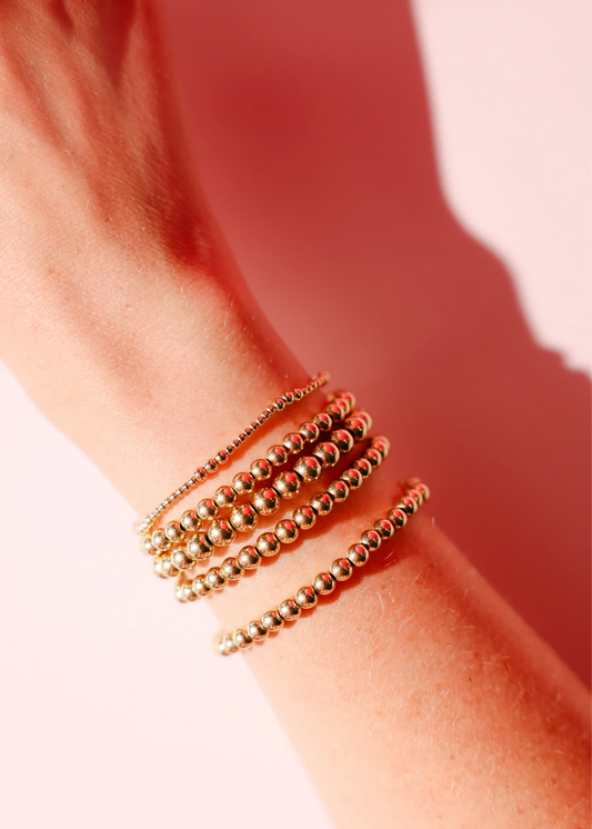 Stack of gold beaded bracelets on a wrist.