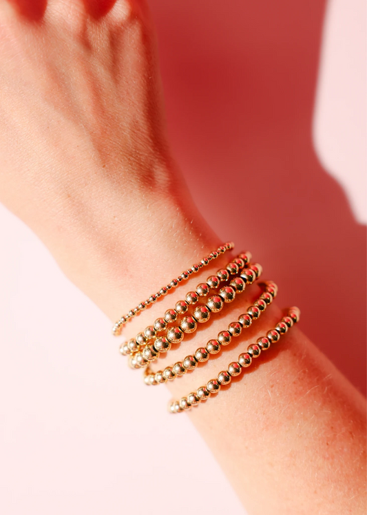 Stack of gold beaded bracelets on a wrist.