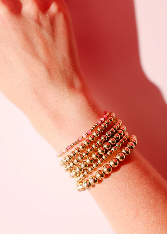 Layered pink and gold bracelets worn together on a wrist.