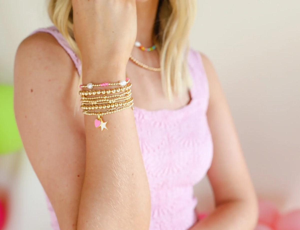 Pink, pearl and gold bracelets layered on a wrist beside a pink top.