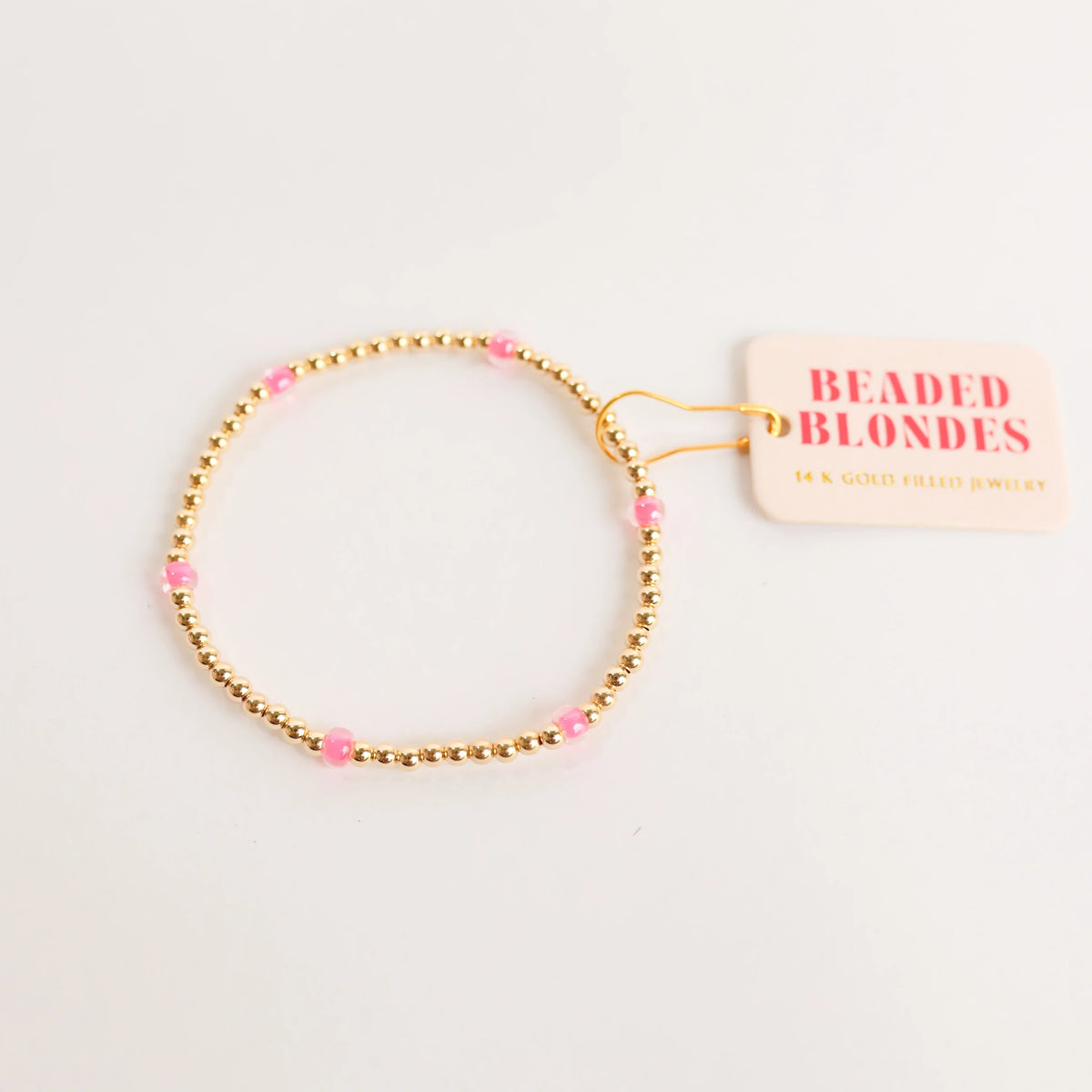 Hot Pink Poppi Bracelet shown in a round shape with pink accents, gold beads and a Beaded Blondes tag.