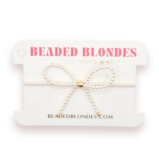 Beaded Blondes Pearl Bow Bracelet with a white pearl bow and gold details on a display card.