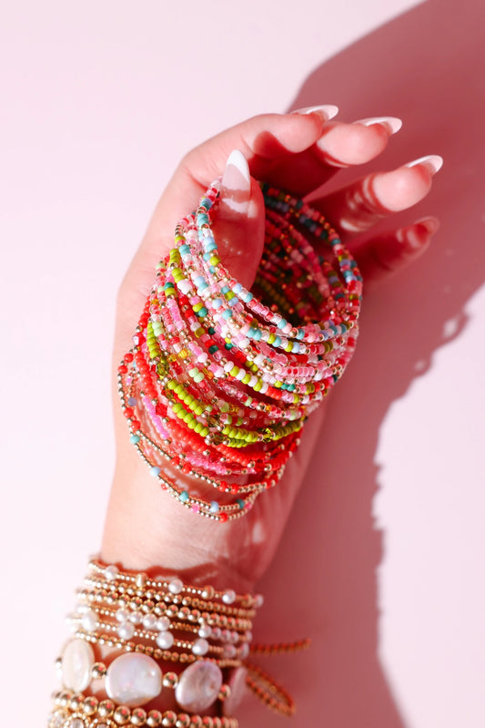 Hand holding several colorful beaded bracelets with jewelry tags.