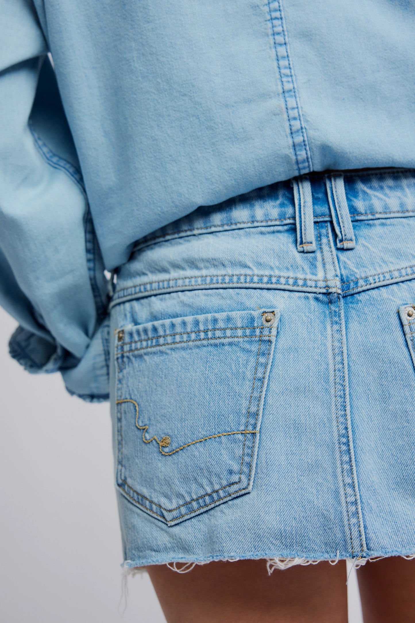 Close-up of a person wearing a light blue denim jacket and skirt on a plain background