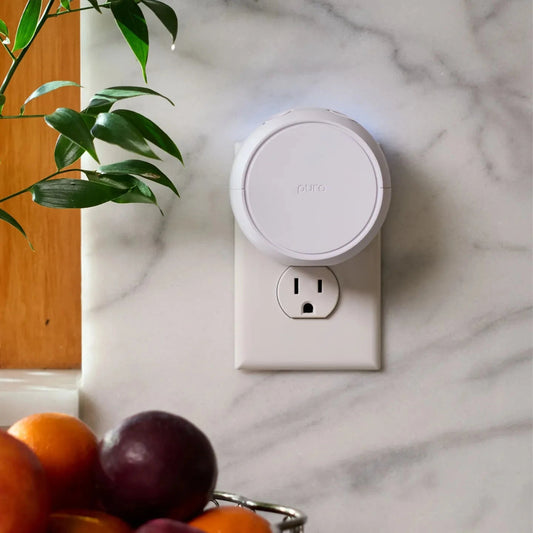 White Pura v5 smart home diffuser plugged into an outlet on a marble wall.