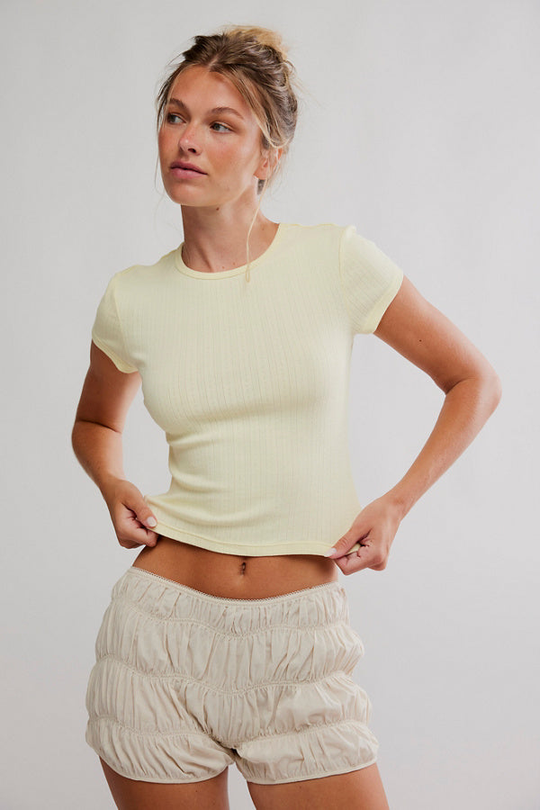 Woman wearing a light green top and beige shorts against a plain background