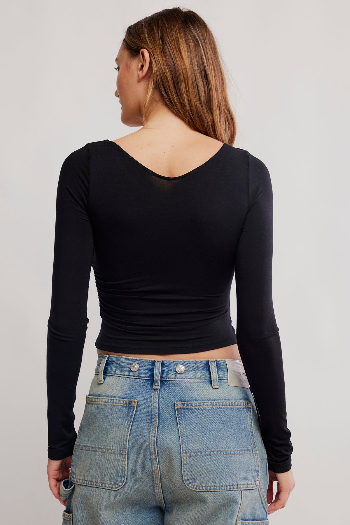 Person wearing a black long-sleeve top and blue jeans on a plain background