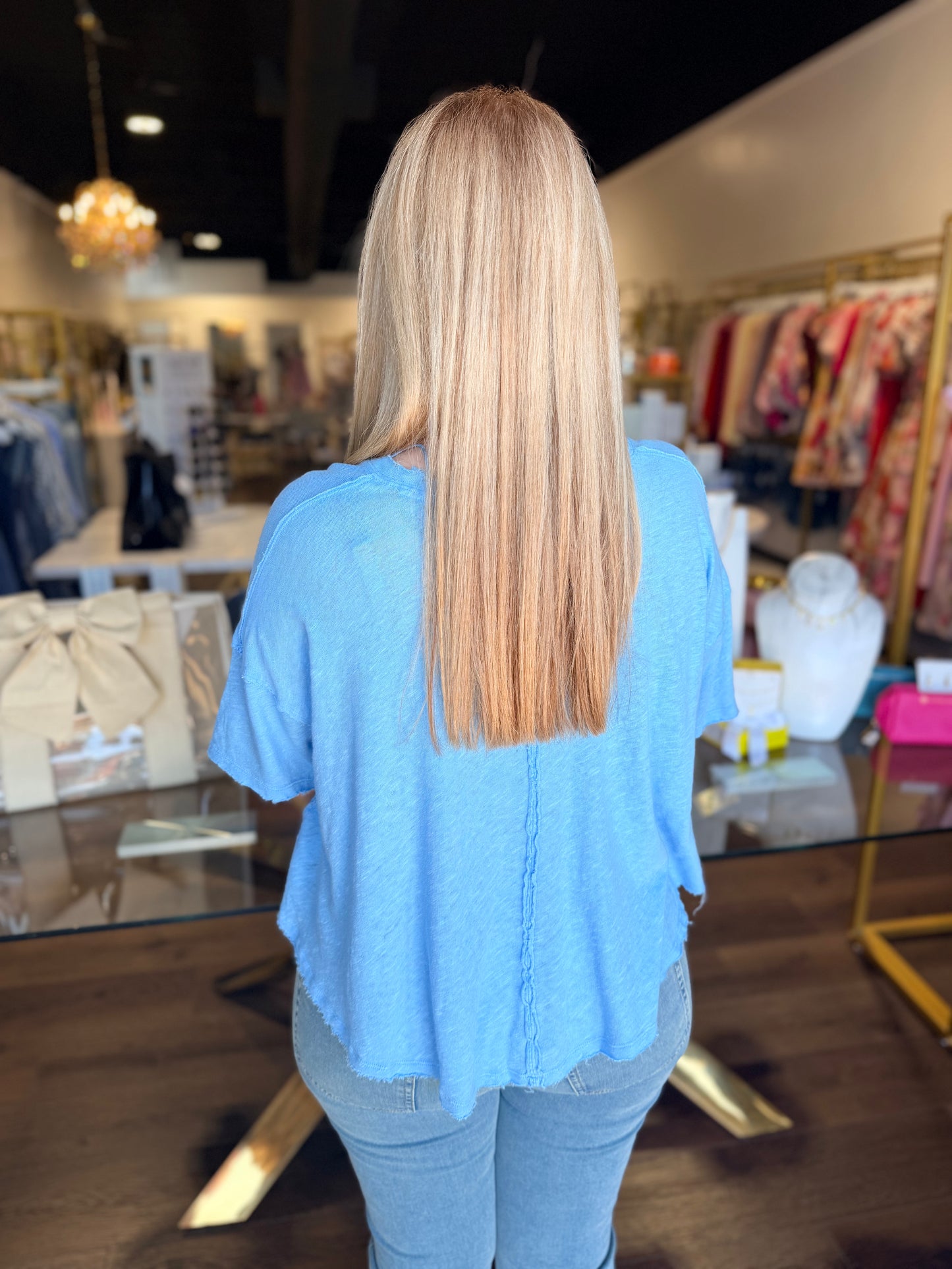 Person wearing a blue shirt in a store setting with clothing racks and displays.